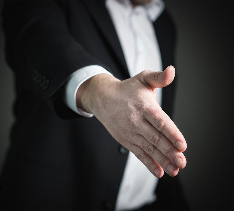 A man in a suit extends his hand to offer a handshake to a new hire