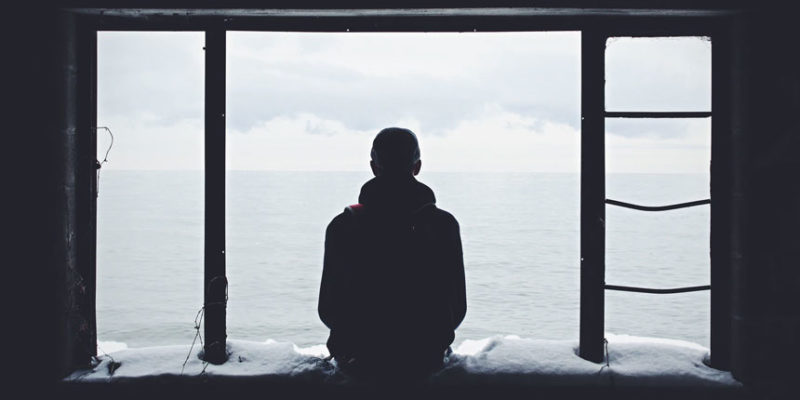 A man looks out onto the ocean from an open window