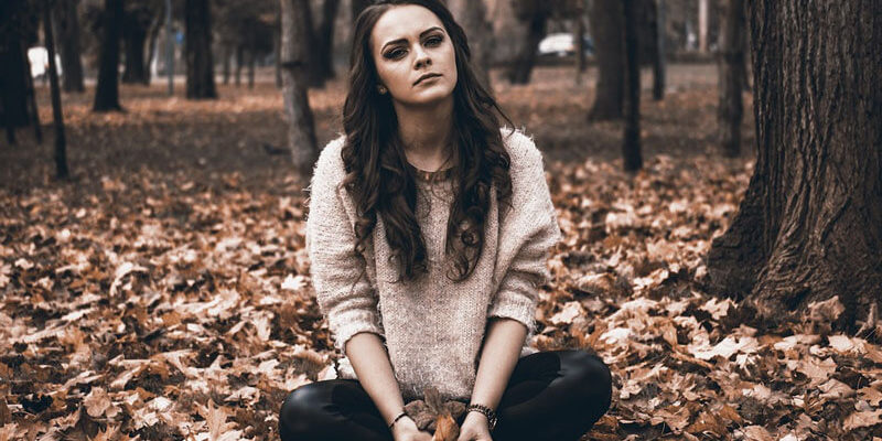 A melancholic teenager sitting in a field full of fallen leaves