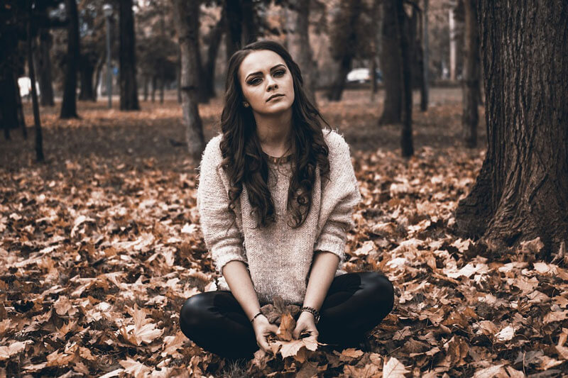 A melancholic teenager sitting in a field full of fallen leaves