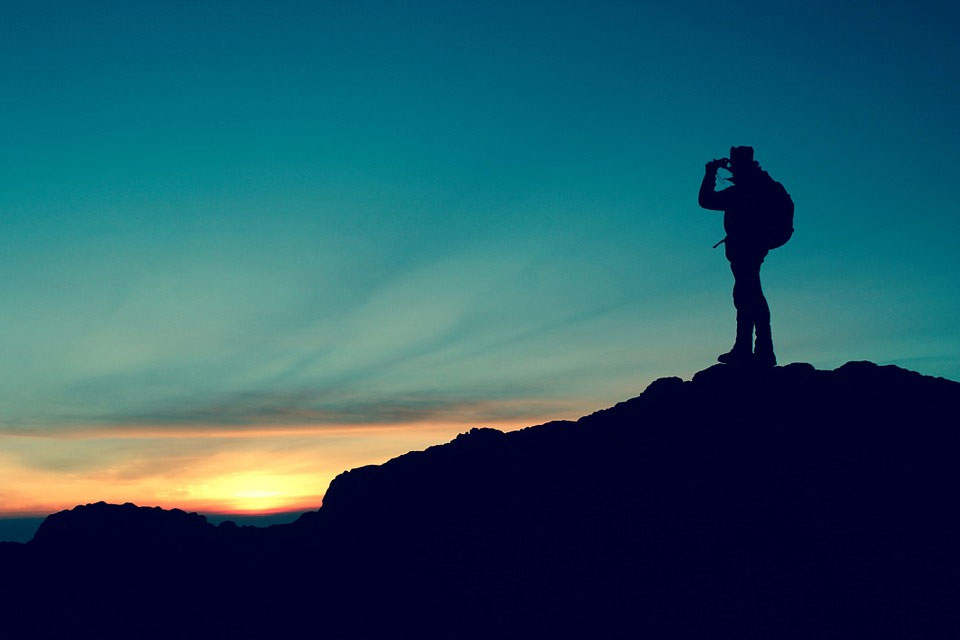 A hiker standing on top of a hill at twilight, looking off into the distance