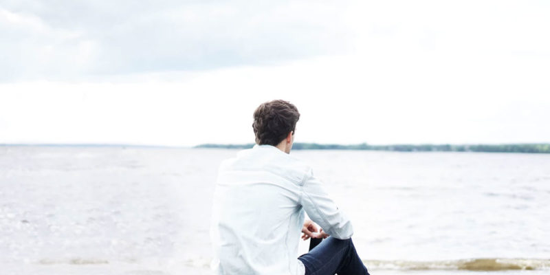 A man sitting alone on a lakeshore