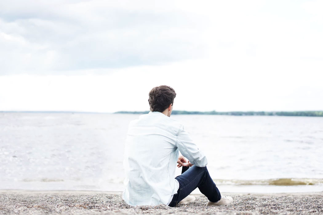 A man sitting alone on a lakeshore