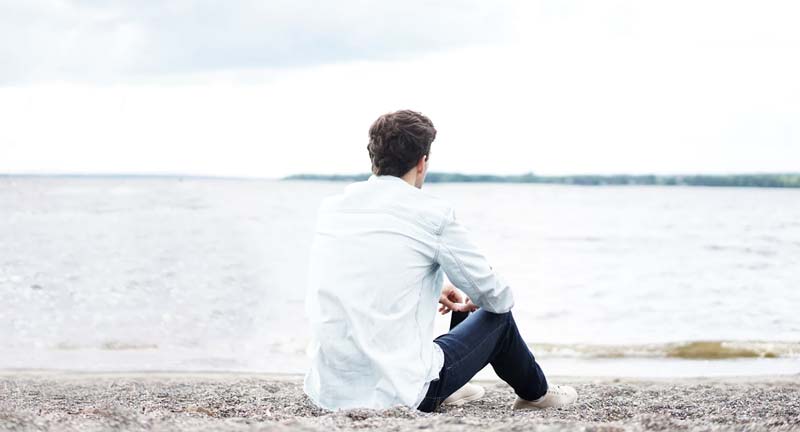 Man sits on rocky beach near water