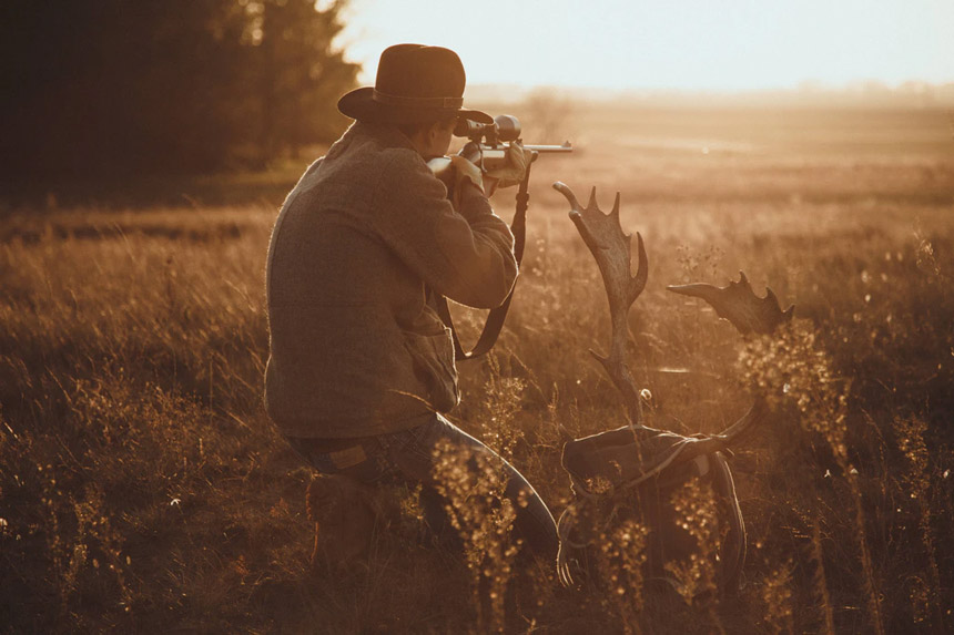 A hunter takes aim with his rifle on an open plain.